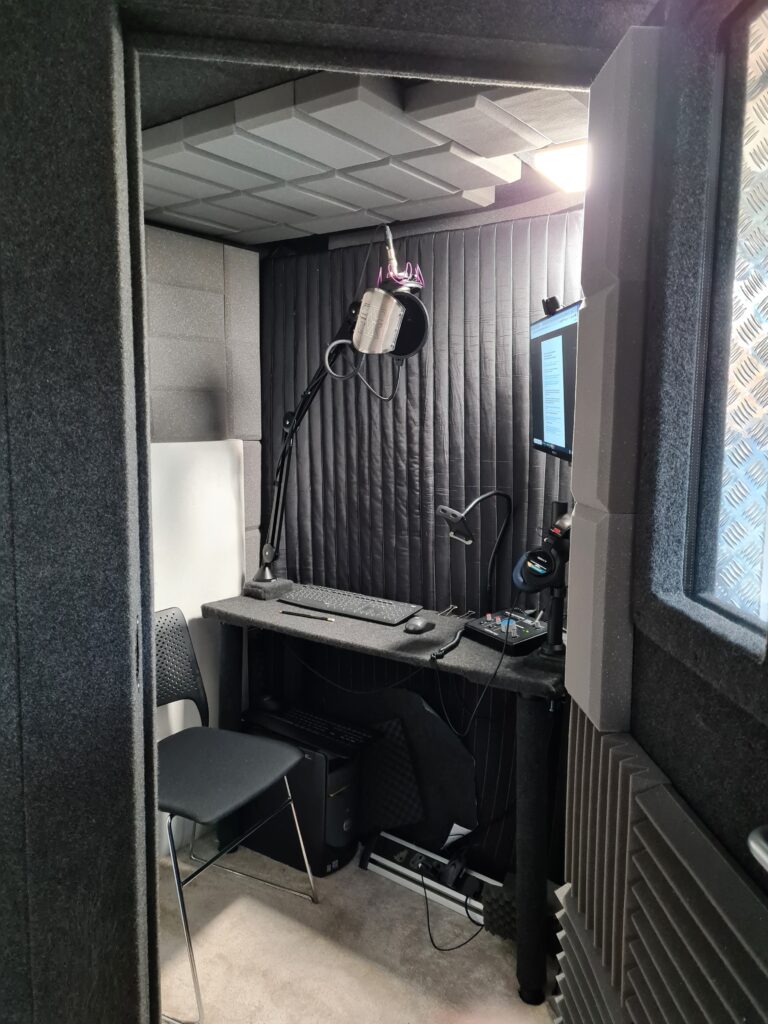 View into the voice actor's recording booth in the home studio, through the booth's open door, showing desk, screen, microphone and acoustic treatment